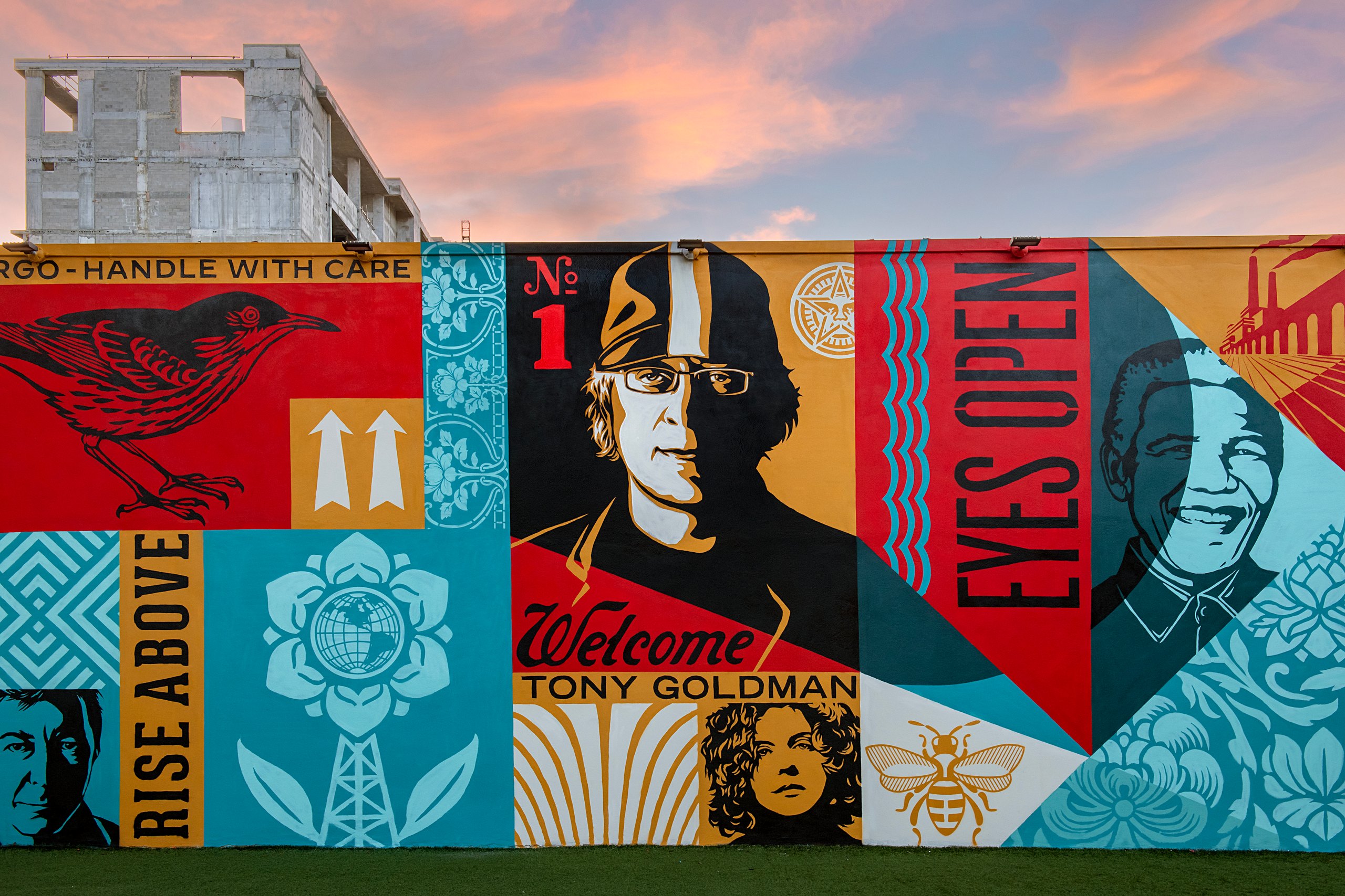 Colorful Wynwood Walls murals featuring a portrait of Tony Goldman beneath a sunset sky.